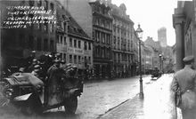 Retuschierte Aufnahme von der Niederschlagung der Räterepublik 1919 im Bereich Unterer Anger 12/13 in München. Am rechten Bildrand wurde die weibliche Begleitung des Soldaten sowie eine weitere Person entfernt, um den Eindruck entstehen zu lassen, dass die Aufnahme im Zuge der Niederschlagung der Räterepublik durch Regierungstruppen entstand. (Bayerische Staatsbibliothek, Bildarchiv hoff-70953)