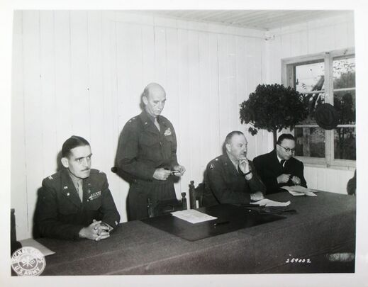 Rede von Generalmajor Horace L. McBride am 10. Oktober 1946 zur Übertragung der Internierungslager an die bayerischen Behörden. Anwesend von links: Colonel Charles Pennoyer Bixel, General McBride, Brigadegeneral Walter J. Muller, Anton Pfeiffer. (National Archives Washington, SC 259002 / Stadtarchiv Moosburg)