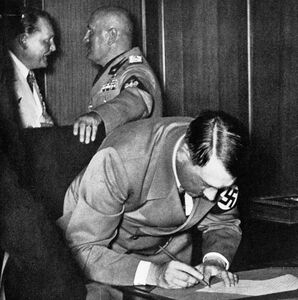 Adolf Hitler beim Unterzeichnen des Abkommens am 30. September 1938. Links im Hintergrund in weißer Uniform Hermann Göring im Gespräch mit Benito Mussolini. (Bayerische Staatsbibliothek, Bildarchiv hoff-20608)