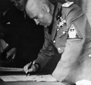 Benito Mussolini unterzeichnet das Münchener Abkommen, im Hintergrund assistiert Paul Schmidt, offizieller Dolmetscher Hitlers seit 1935 und Mitglied der SS seit 1937. (Bayerische Staatsbibliothek, Bildarchiv hoff-20624)