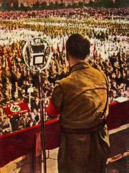 Adolf Hitler spricht anlässlich des Reichstagswahlkampfes am 24. Juli 1932 in Bochum (Nordrhein-Westfalen). Zigarettensammelbild. Hoffmann kooperierte seit 1933 mit dem Reemtsma-Konzern und lieferte das Bildmaterial für mehrere Sammelalben von Zigarettenbildern mit NS-Propaganda. Durch die seit den 1920ern weit verbreiteten Sammelalben erreichten Hoffmanns Zigarettenbilder Millionenauflagen. (Bayerische Staatsbibliothek, Bildarchiv hoff-7296)