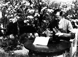 Der Dichter und Schriftsteller Joseph Maria Lutz (1893-1970) mit Schreibmaschine im Garten, Foto um 1934. (Bayerische Staatsbibliothek, Bildarchiv)